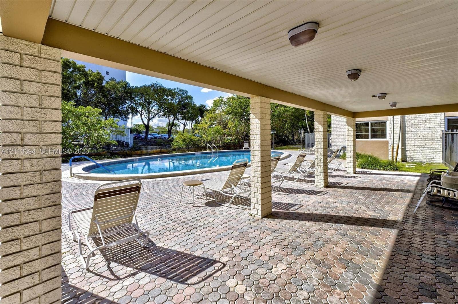 124 NE 19th Court, #108B, Wilton Manors, FL 33305 Covered patio featuring brick-paver flooring and structural brick columns, opening to a swimming pool with a concrete pool deck
