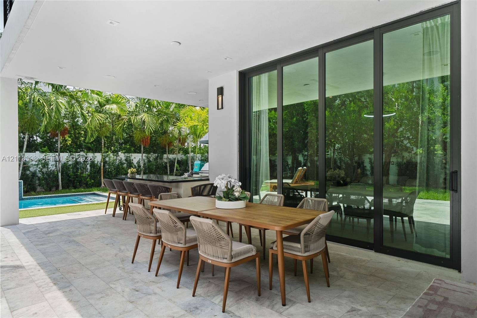 6814 NW 104th Court, #6814, Doral, Doral, FL 33178 Covered patio featuring stone-tile flooring, floor-to-ceiling glass sliding doors, recessed lighting, and a built-in outdoor kitchen with a stone countertop