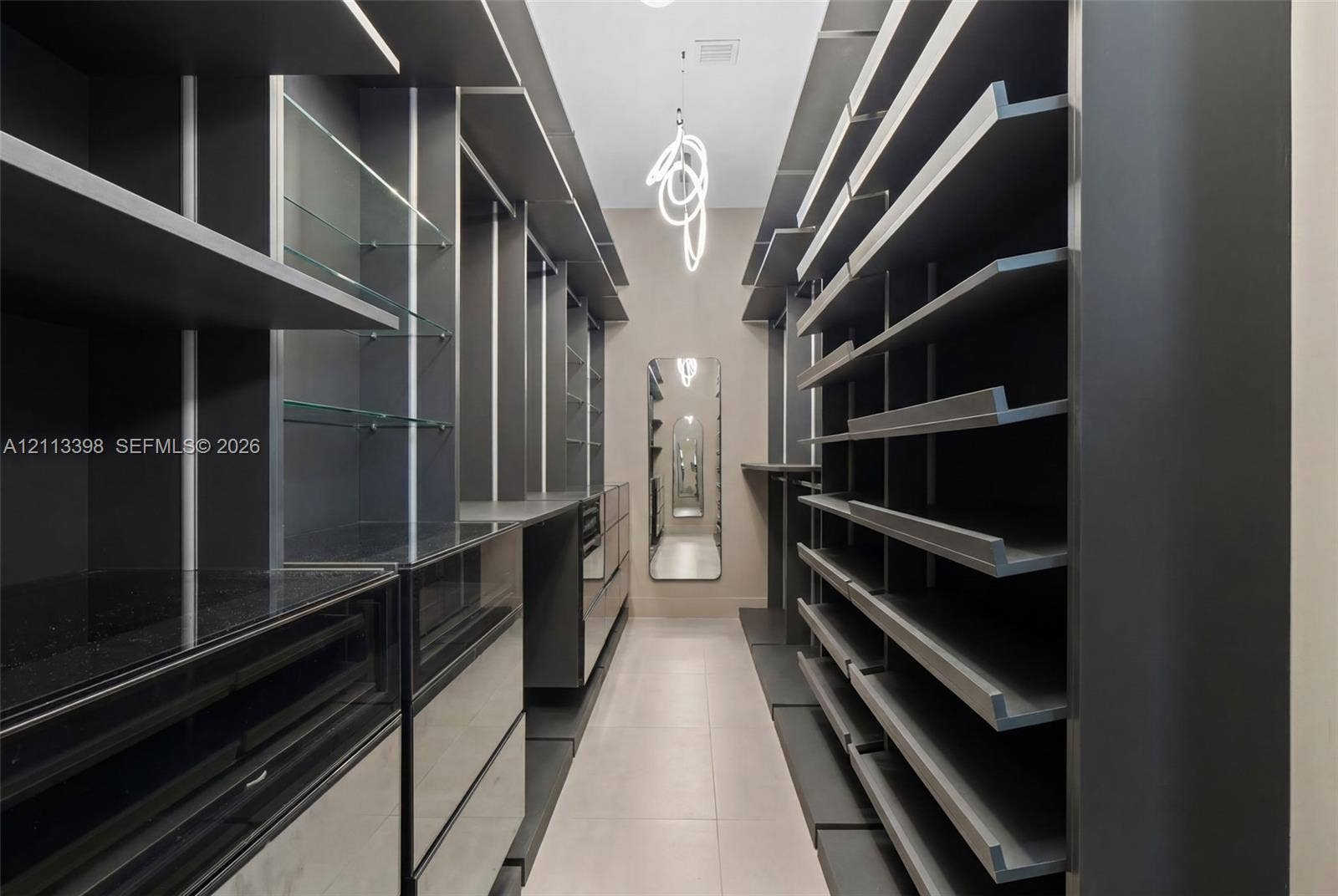 6814 NW 104th Court, #6814, Doral, Doral, FL 33178 Custom walk-in storage area featuring dark-toned built-in cabinetry, integrated glass shelving, sleek flat-front drawers, a full-length wall mirror, and a contemporary sculptural pendant fixture