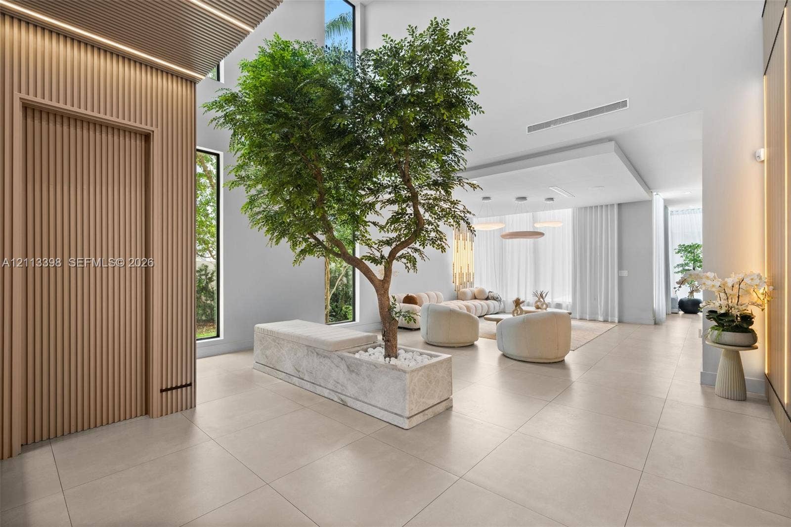 6814 NW 104th Court, #6814, Doral, Doral, FL 33178 Open-concept interior featuring vertical wood-slat wall paneling, floor-to-ceiling windows, large-format tile flooring, and a built-in stone planter