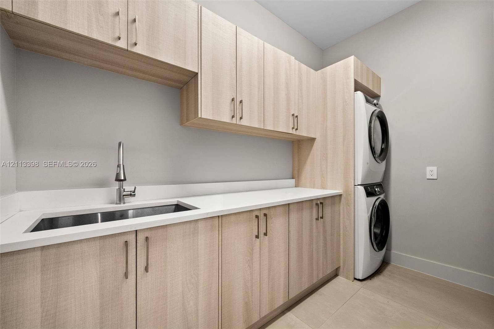 6814 NW 104th Court, #6814, Doral, Doral, FL 33178 Laundry room featuring light wood-finish cabinetry, white solid-surface countertops, an undermount stainless steel sink with a high-arch pull-down faucet, and a stacked washer and dryer unit