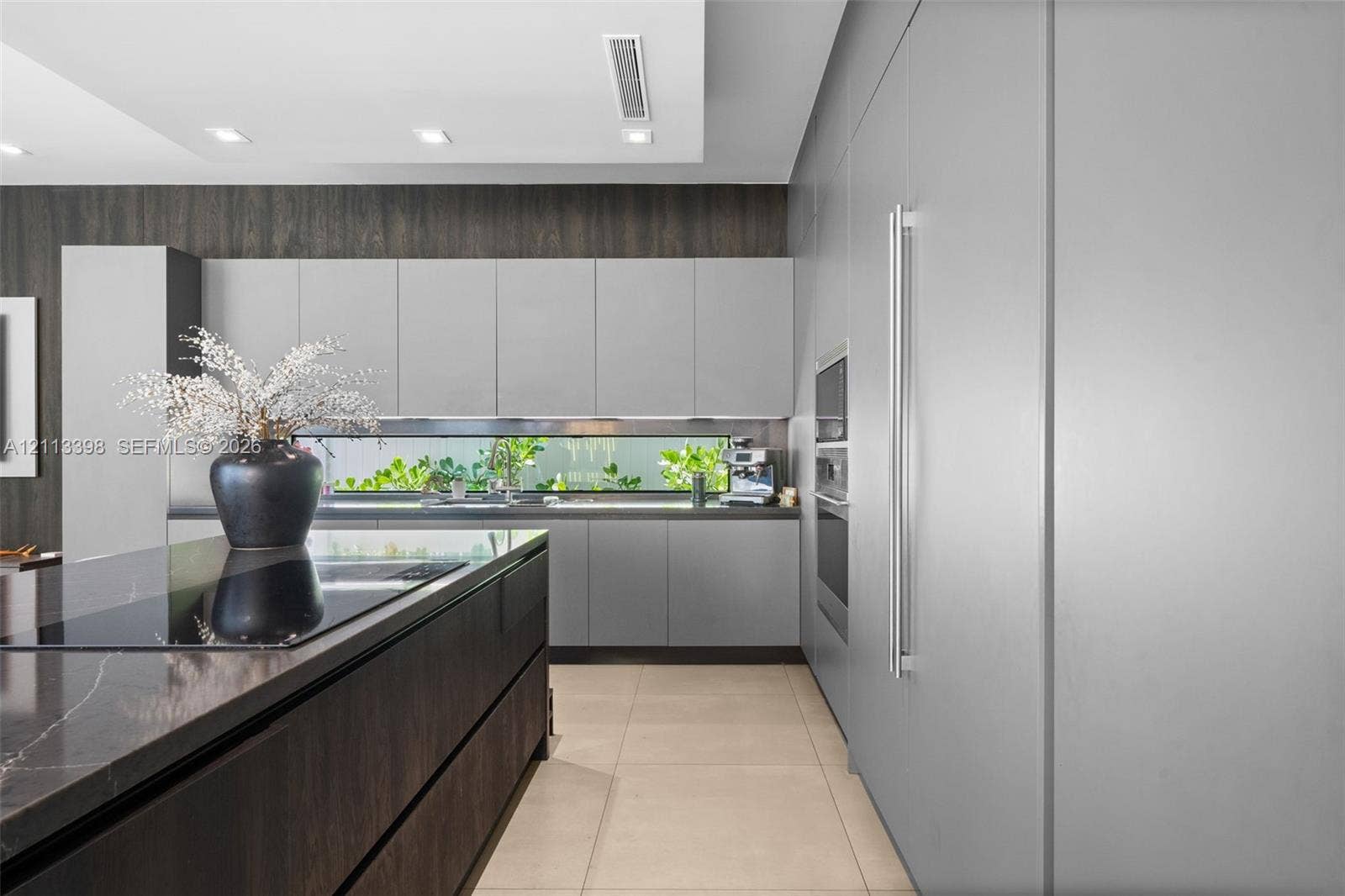 6814 NW 104th Court, #6814, Doral, Doral, FL 33178 Contemporary kitchen featuring flat-panel cabinetry, a dark-toned center island with a stone-surface countertop, integrated stainless steel appliances, a linear backsplash window, and large-format tile flooring