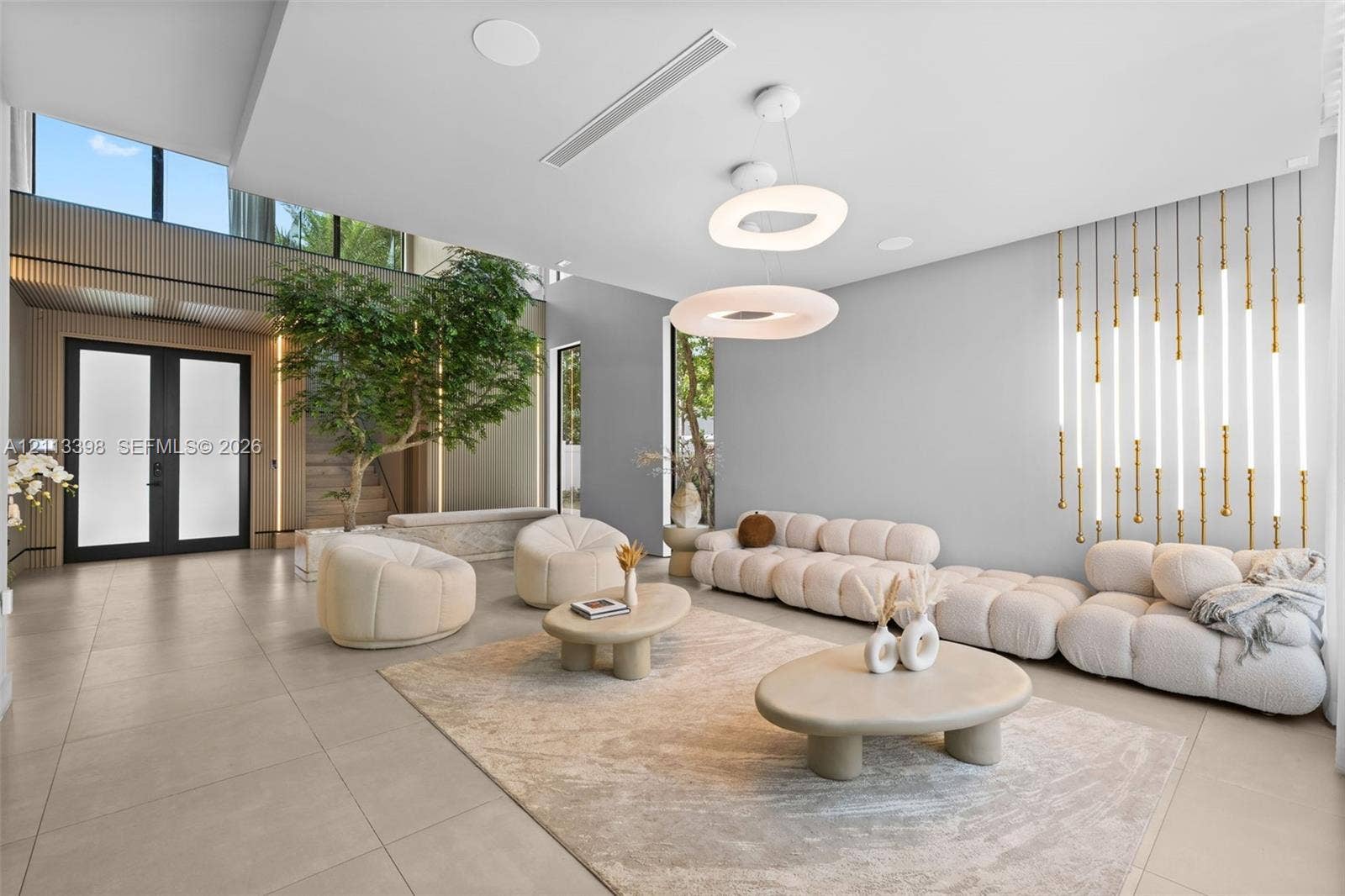 6814 NW 104th Court, #6814, Doral, Doral, FL 33178 Open-concept interior featuring large-format tile flooring, double-height ceilings, vertical wall-mounted linear light fixtures, circular tiered pendant lighting, and slatted wood-finish wall accents