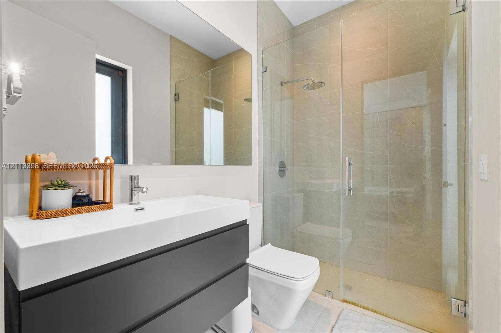 6814 NW 104th Court, #6814, Doral, Doral, FL 33178 Wall-mounted dark cabinetry with a white rectangular sink basin, large frameless wall mirror, walk-in glass-enclosed shower, and neutral-toned wall tiling