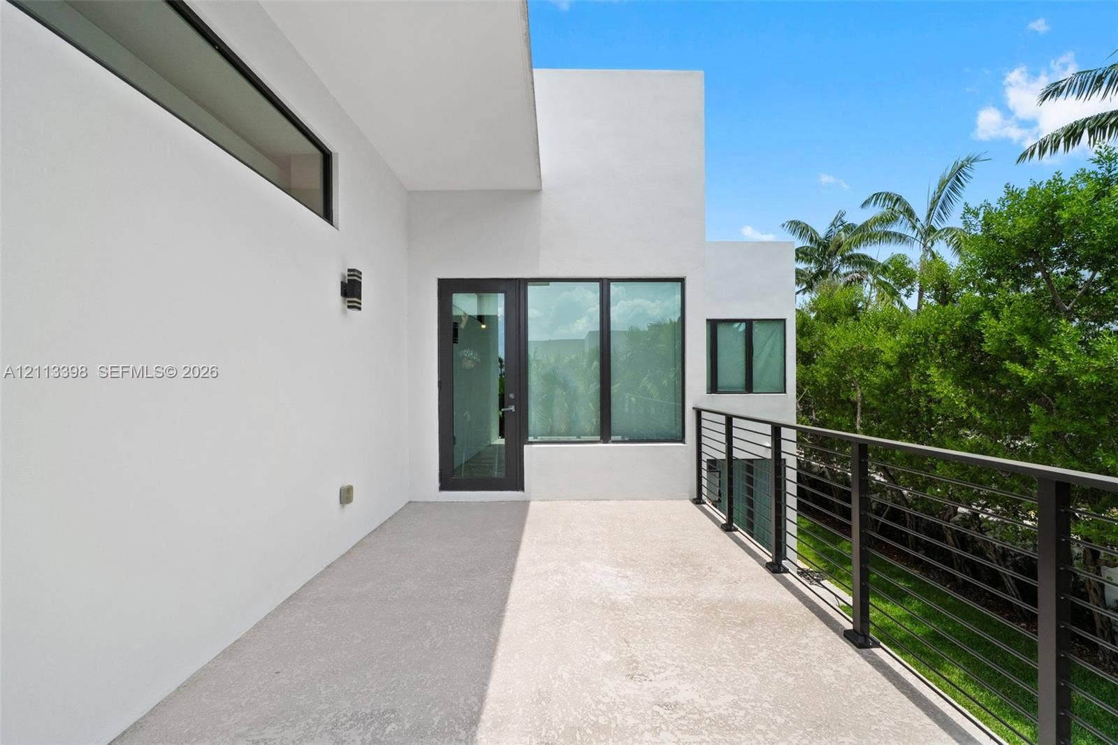 6814 NW 104th Court, #6814, Doral, Doral, FL 33178 Covered exterior terrace featuring a smooth concrete floor, minimalist white stucco exterior walls, dark-framed expansive windows, and a metal horizontal-bar railing