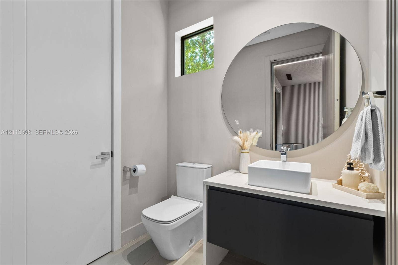 6814 NW 104th Court, #6814, Doral, Doral, FL 33178 Floating dark-finish vanity with a white rectangular vessel sink, solid-surface countertop, circular frameless mirror, and dual-flush toilet