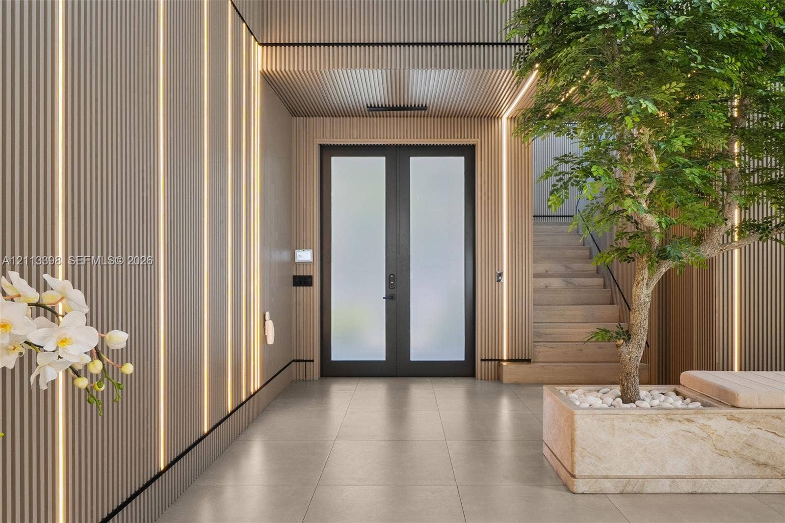 6814 NW 104th Court, #6814, Doral, Doral, FL 33178 Entryway featuring vertical wood-slat wall paneling, integrated linear lighting, large-format tile flooring, double doors with frosted glass, and a built-in stone planter