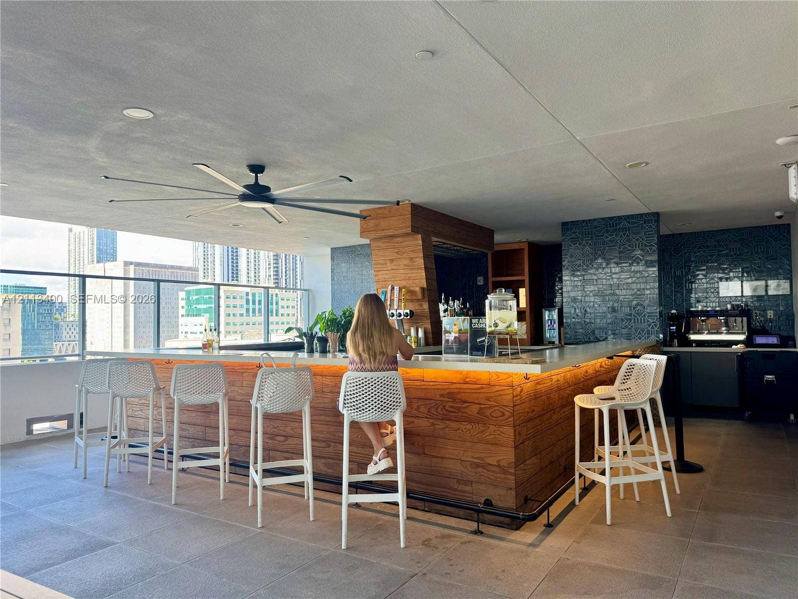 227 NE 2nd Street, #2105, Miami, FL 33132 Outdoor bar featuring wood-paneled cabinetry, stone countertop with integrated under-cabinet lighting, glass-tiled backsplash, and a large overhead ceiling fan on a covered terrace