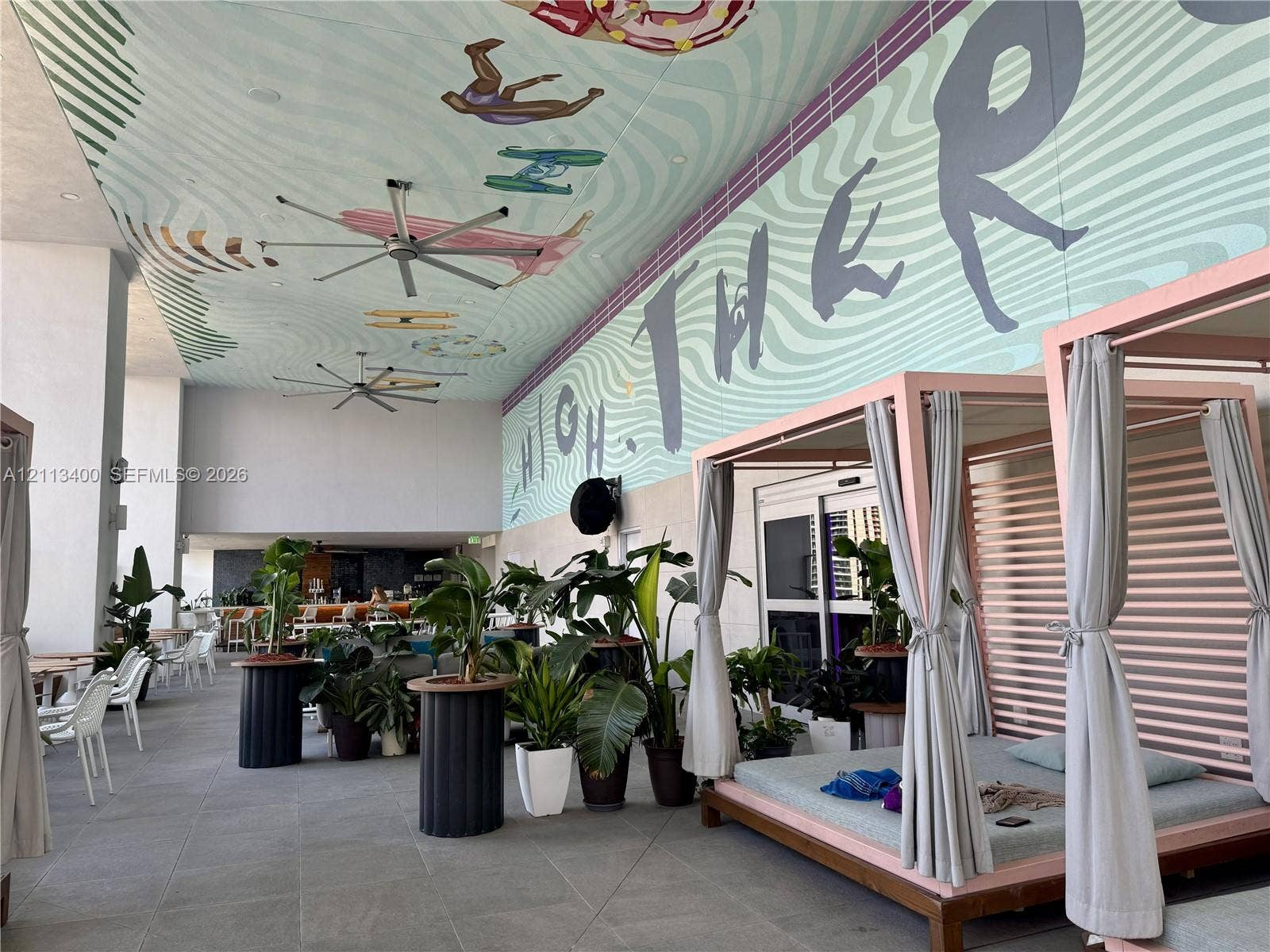 227 NE 2nd Street, #2105, Miami, FL 33132 Covered outdoor lounge area featuring large-format stone flooring, ceiling-mounted industrial fans, and a decorative ceiling mural