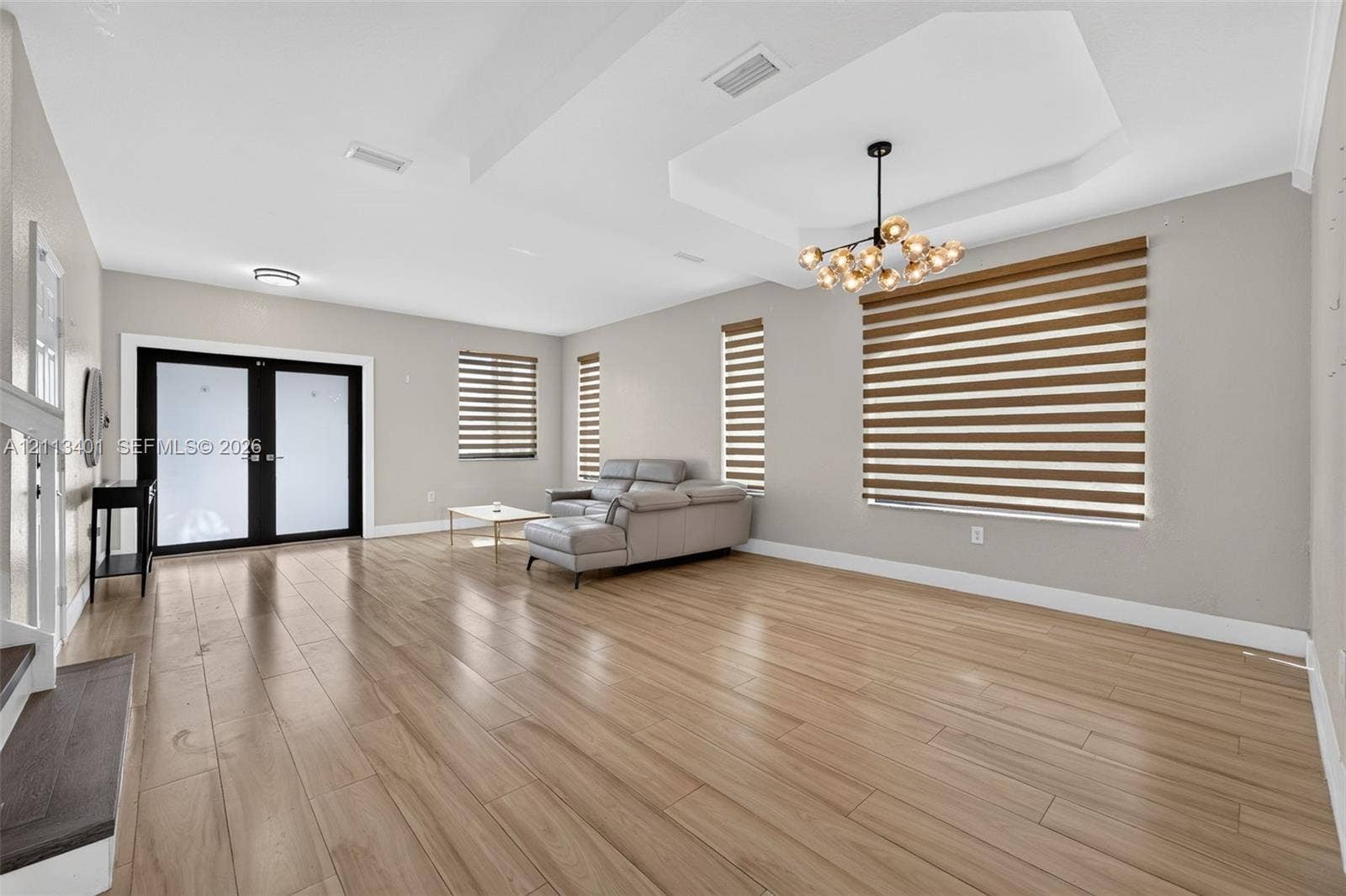15891 SW 139th Street, Miami, Miami, FL 33196 Open-concept room featuring tray ceilings, wood-finish flooring, a multi-globe chandelier, double-entry glass doors, and layered window shades