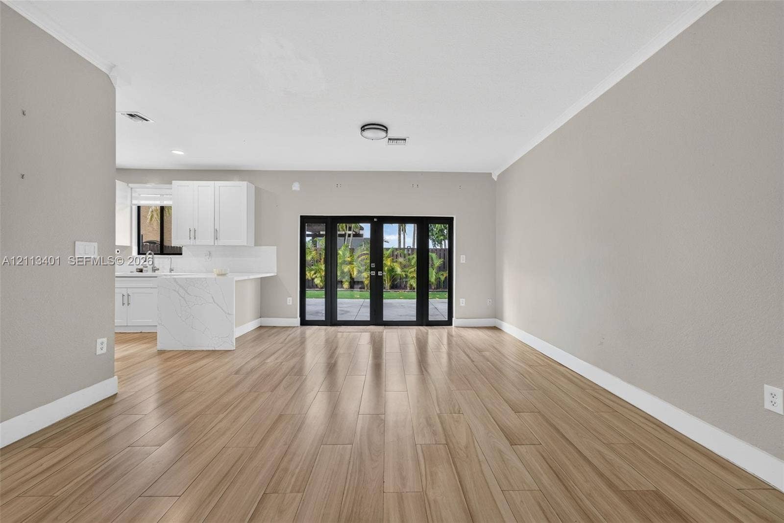 15891 SW 139th Street, Miami, Miami, FL 33196 Open-concept area featuring wood-finish flooring, white cabinetry, a stone-finish waterfall-edge peninsula, and black-framed glass french doors