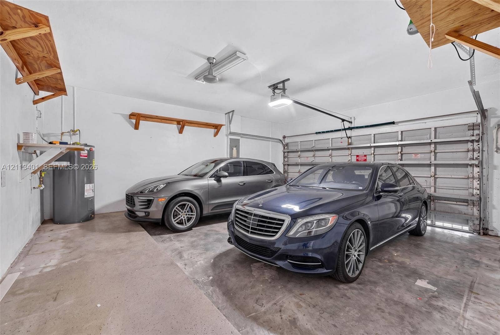 15891 SW 139th Street, Miami, Miami, FL 33196 Two-car garage featuring a concrete floor, sectional overhead door, built-in wooden wall shelving, and a dedicated water heater
