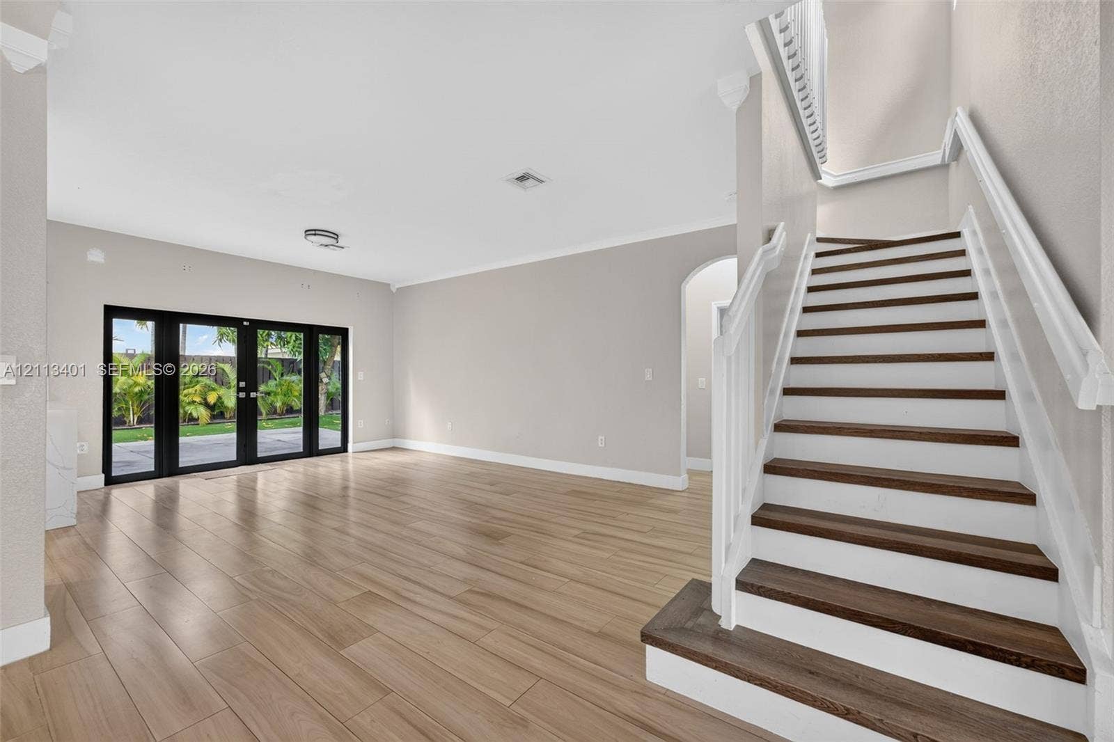 15891 SW 139th Street, Miami, Miami, FL 33196 Open-concept interior featuring wood-finish flooring, a staircase with white balusters and dark wood-finish treads, crown molding, and black-framed glass French doors