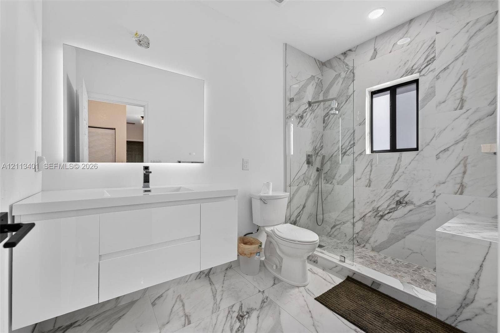 15891 SW 139th Street, Miami, Miami, FL 33196 Floating white vanity with integrated sink, expansive LED-backlit mirror, floor-to-ceiling stone-look wall tiles, walk-in glass-enclosed shower, and matching stone-look tile flooring