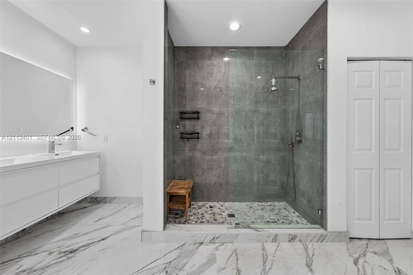 15891 SW 139th Street, Miami, Miami, FL 33196 Floating dual-sink vanity with under-cabinet lighting, walk-in shower with frameless glass enclosure, floor-to-ceiling stone-look wall tile, pebble-texture shower flooring, and large-format porcelain tile flooring