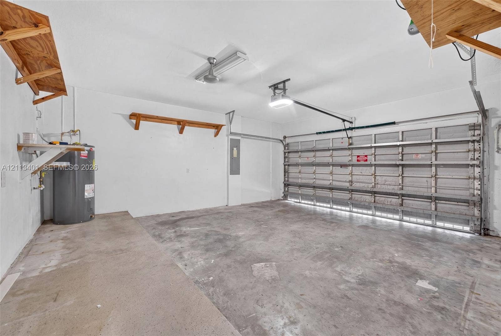 15891 SW 139th Street, Miami, Miami, FL 33196 Two-car garage featuring a concrete floor, built-in wooden wall shelving, overhead fluorescent lighting, an automated door opener, and a dedicated water heater
