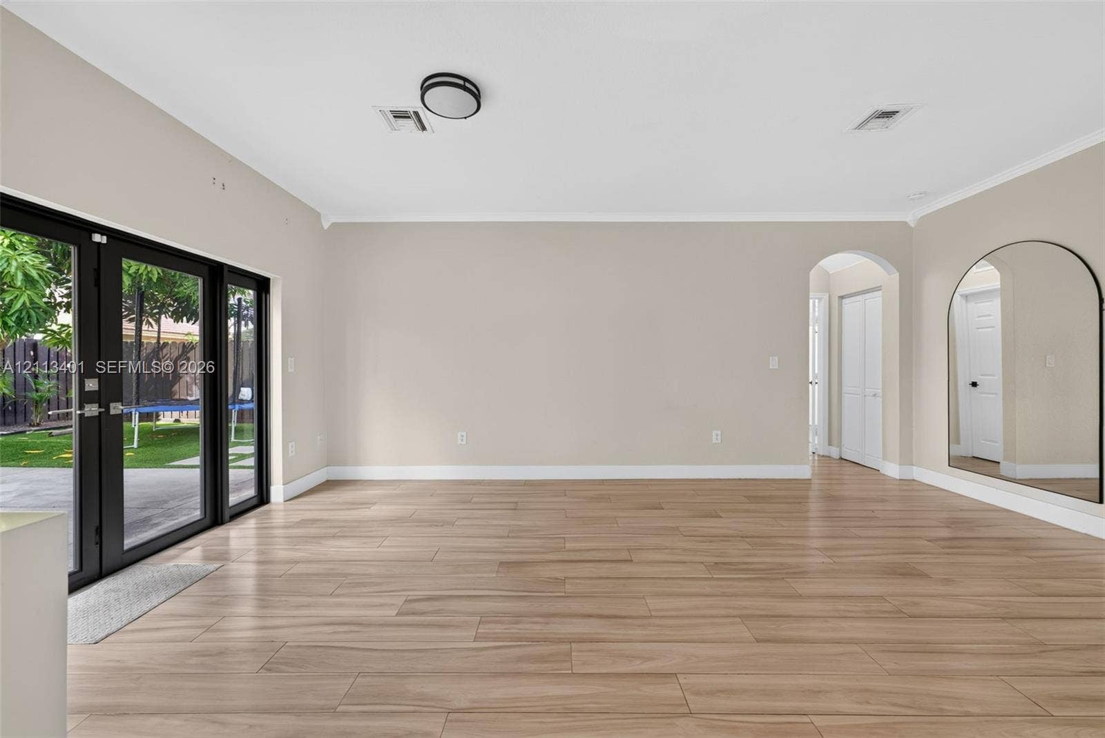 15891 SW 139th Street, Miami, Miami, FL 33196 Open-concept room featuring wood-finish flooring, floor-to-ceiling glass panel double doors with black frames, a high-arched passageway, and a large arched wall-mounted mirror
