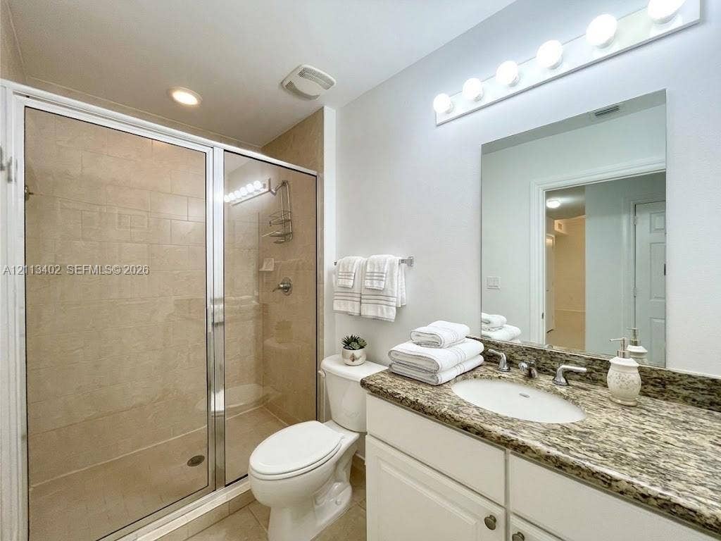3001 NE 185th Street, #207, Aventura, FL 33180 Bathroom featuring a stone-surface vanity with an integrated basin, a walk-in shower with a glass enclosure and tile surround, and a multi-bulb vanity light fixture