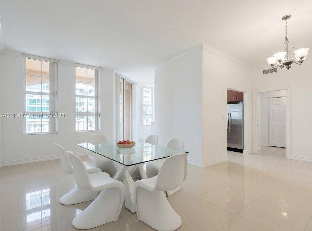 3001 NE 185th Street, #207, Aventura, FL 33180 Bright open living area featuring neutral tile flooring, multi-pane windows, crown molding, and a multi-arm chandelier