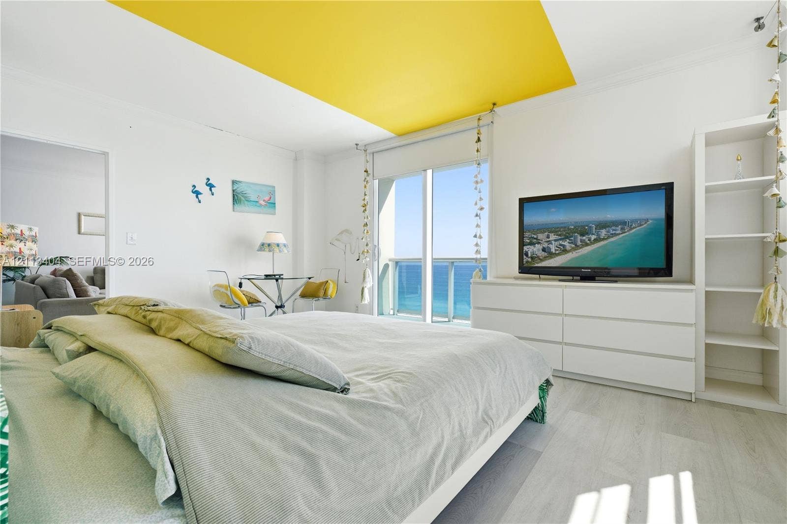 Full-height sliding glass doors with direct ocean access, integrated white built-in shelving, wood-finish flooring, and recessed ceiling feature