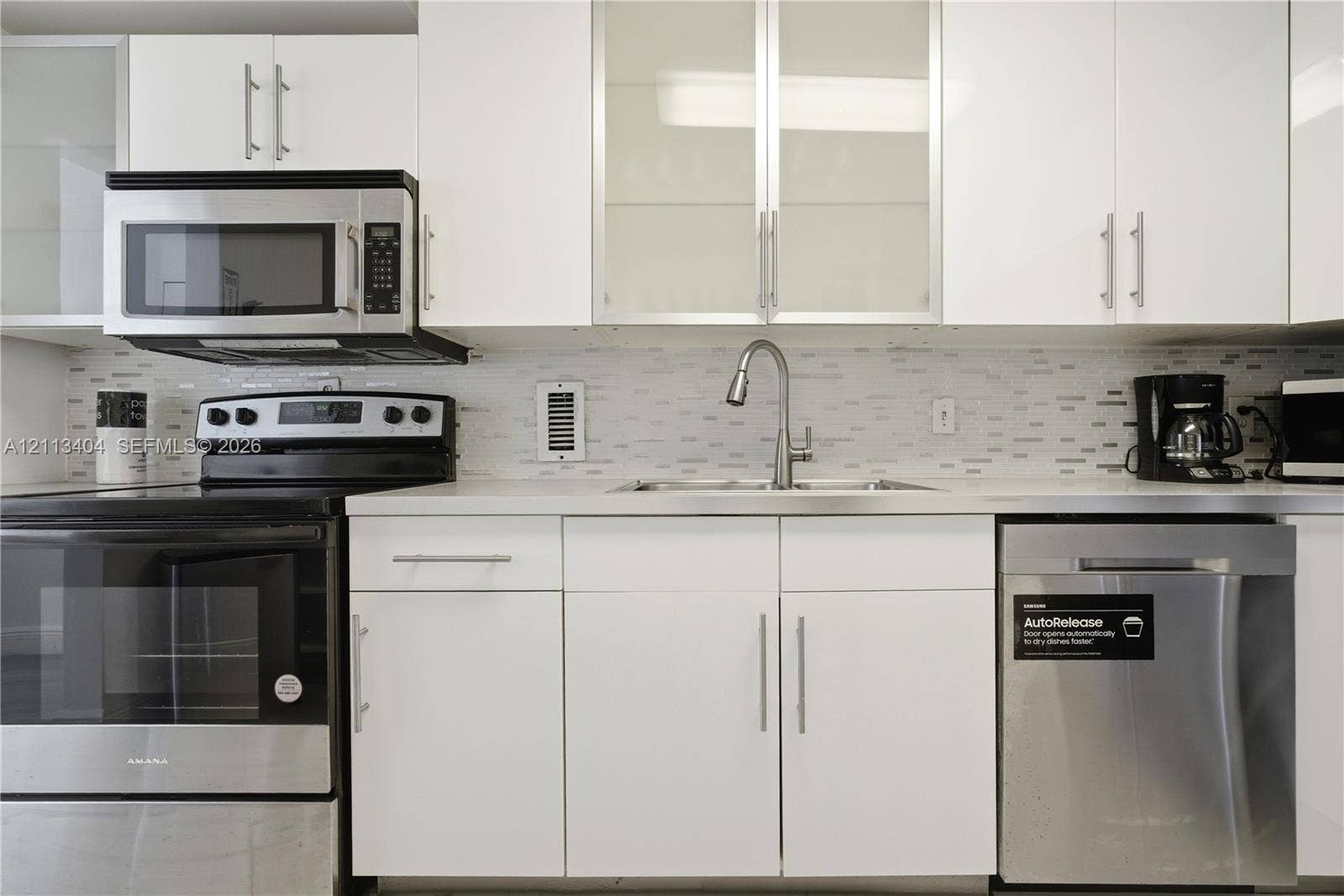 White cabinetry featuring glass-panel upper doors, stainless steel appliances, a multi-tonal linear tile backsplash, and a stainless steel gooseneck faucet