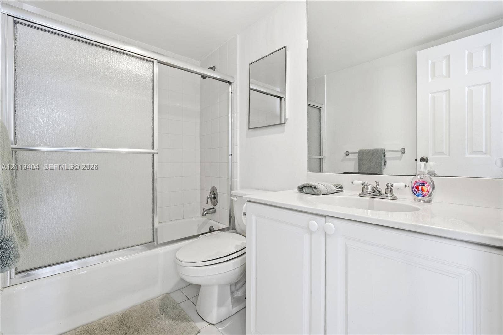 Bathroom featuring a white vanity cabinet with a stone-top integrated sink, chrome dual-handle faucet, oversized wall-mounted mirror, and a shower-tub combination enclosed by sliding glass doors