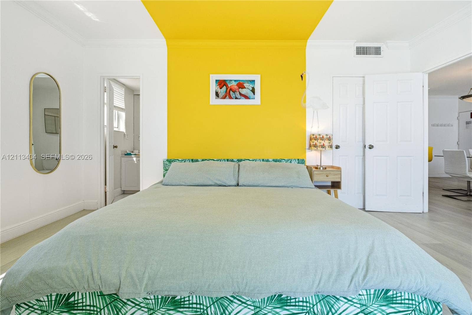 Room featuring wood-finish flooring, a wall-to-ceiling yellow accent, crown molding, and a tall oval wall-mounted mirror