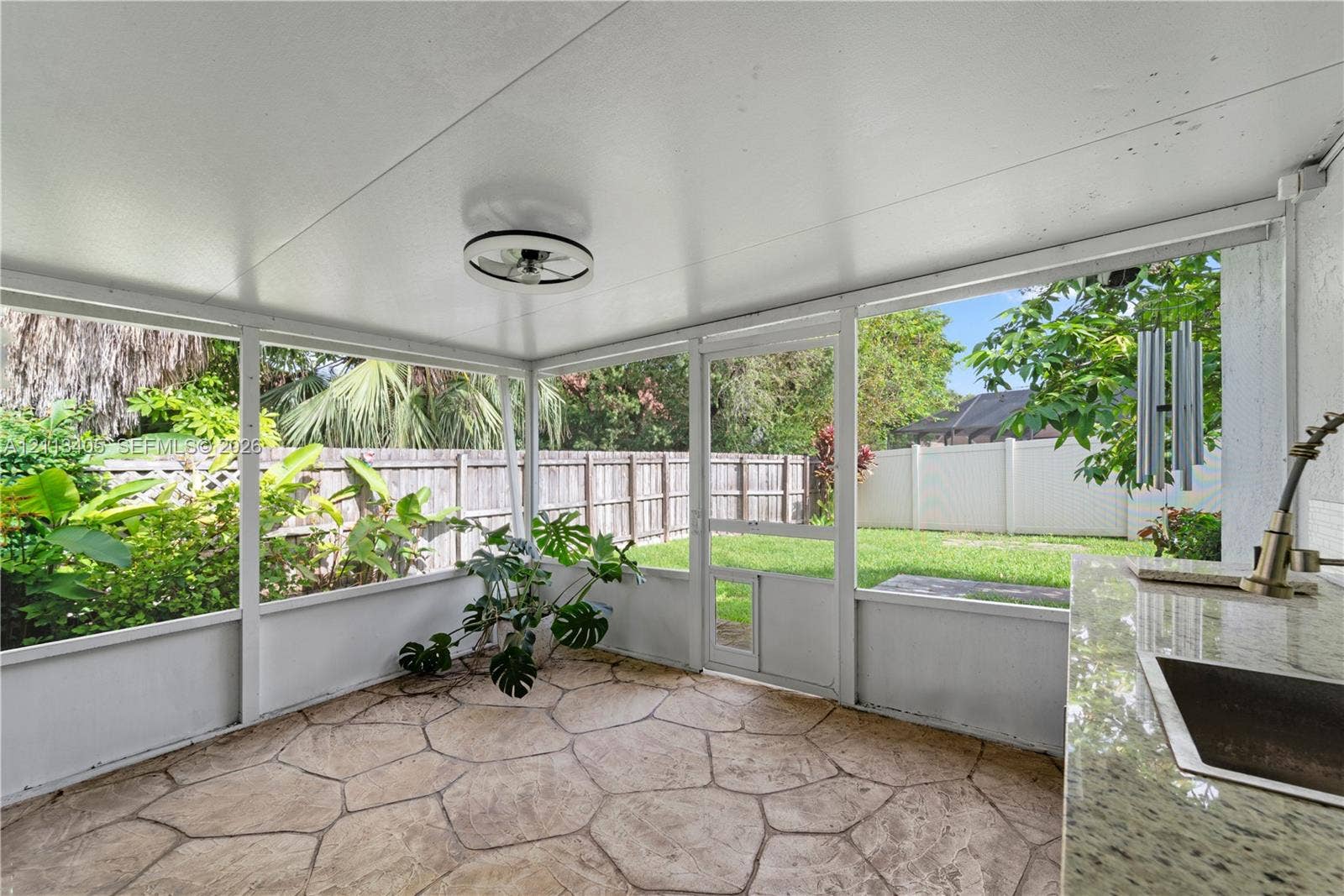 1675 S Goldeneye Lane, Homestead, FL 33035 Screened patio featuring flagstone flooring, a built-in outdoor kitchen with a stone countertop, integrated sink, and ceiling-mounted light fixture