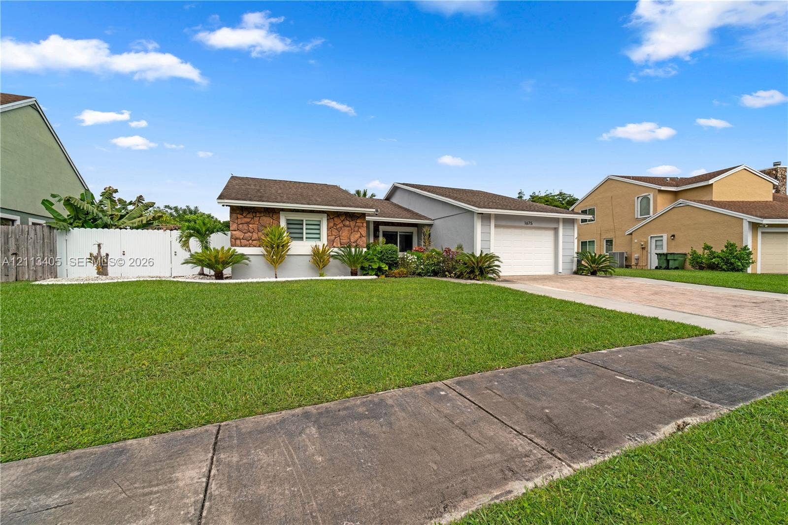 1675 S Goldeneye Lane, Homestead, FL 33035 Single-story exterior featuring a stone-veneer facade, attached garage, concrete driveway, and white privacy fencing