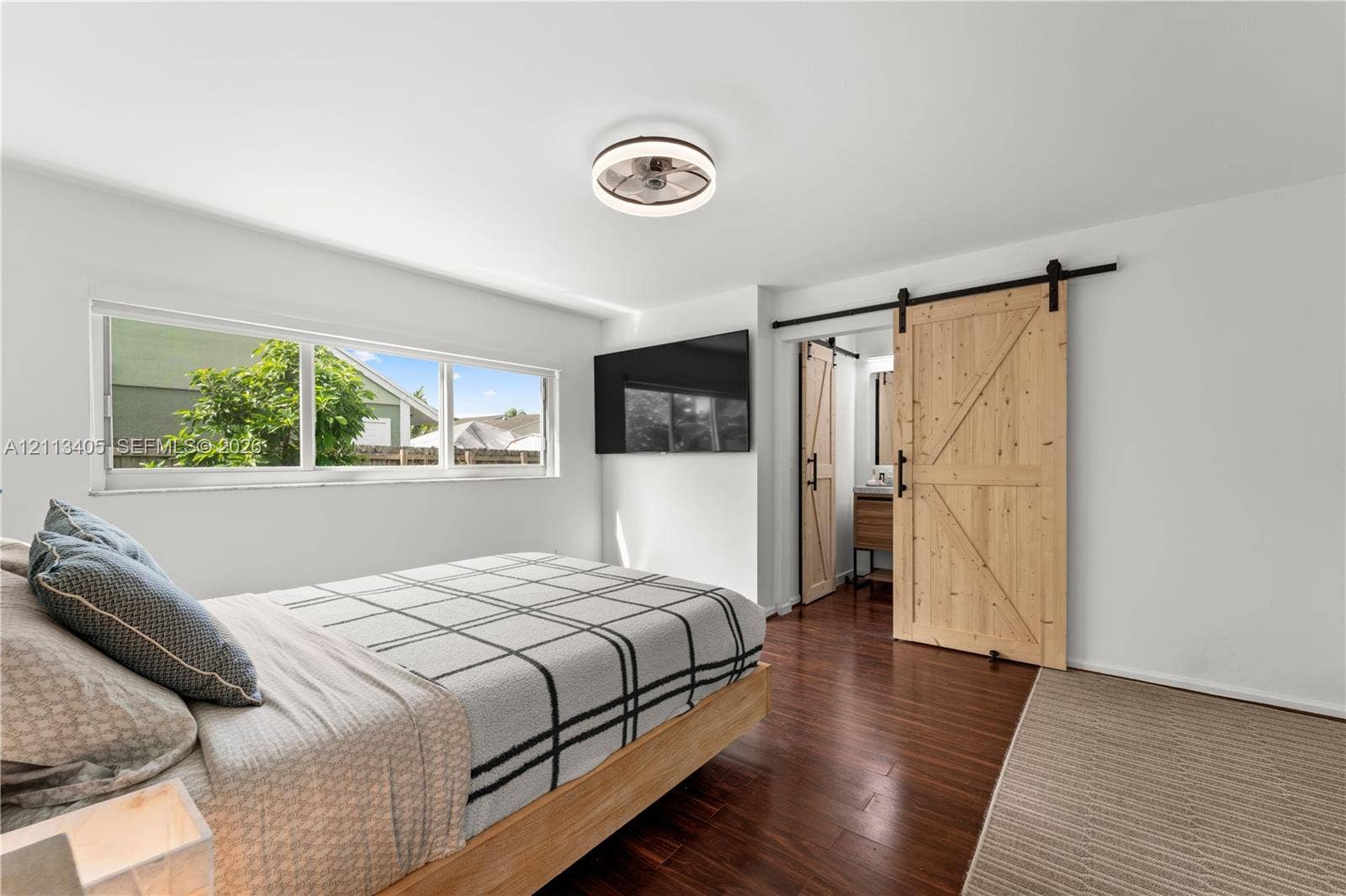 1675 S Goldeneye Lane, Homestead, FL 33035 Wood-finish flooring, sliding wood barn door with matte black hardware, large picture window, and integrated circular ceiling fan with lighting