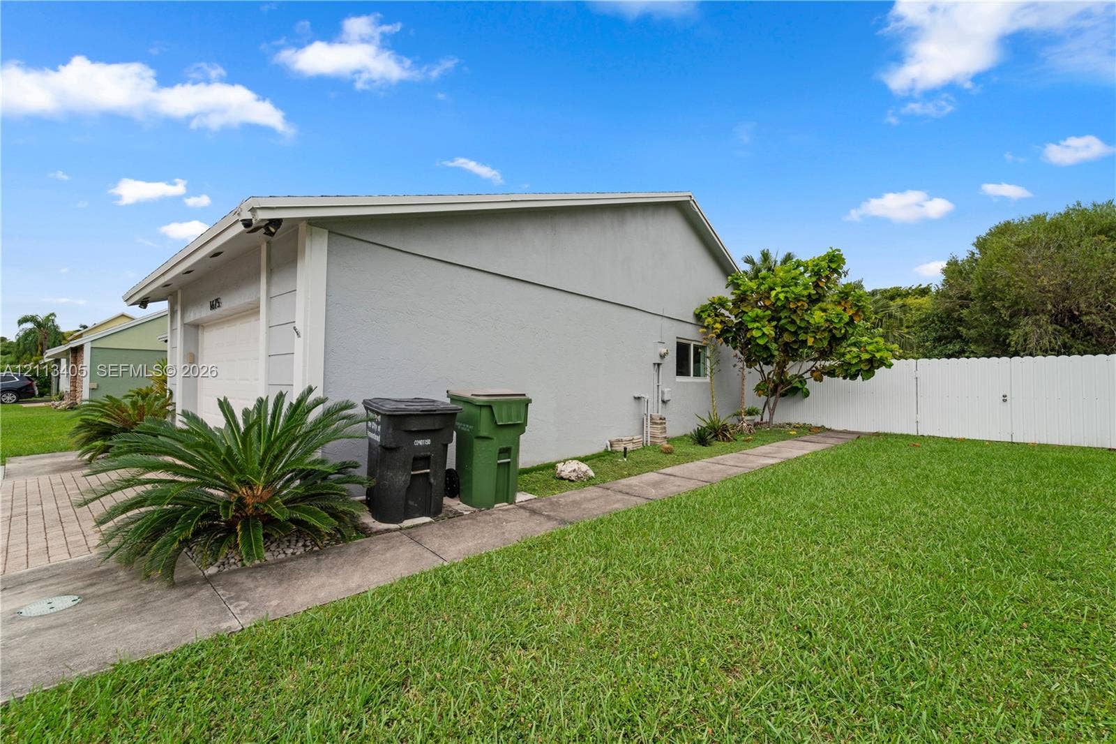 1675 S Goldeneye Lane, Homestead, FL 33035 Stucco exterior featuring a paved walkway, attached garage, and white vinyl perimeter fencing
