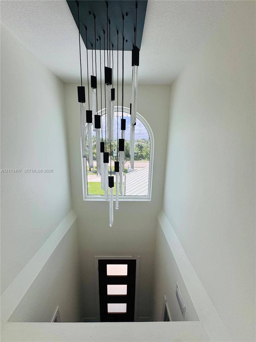 Multi-tiered contemporary chandelier featuring glass and black matte accents, complemented by an arched window and a modern entry door with three rectangular glass panels