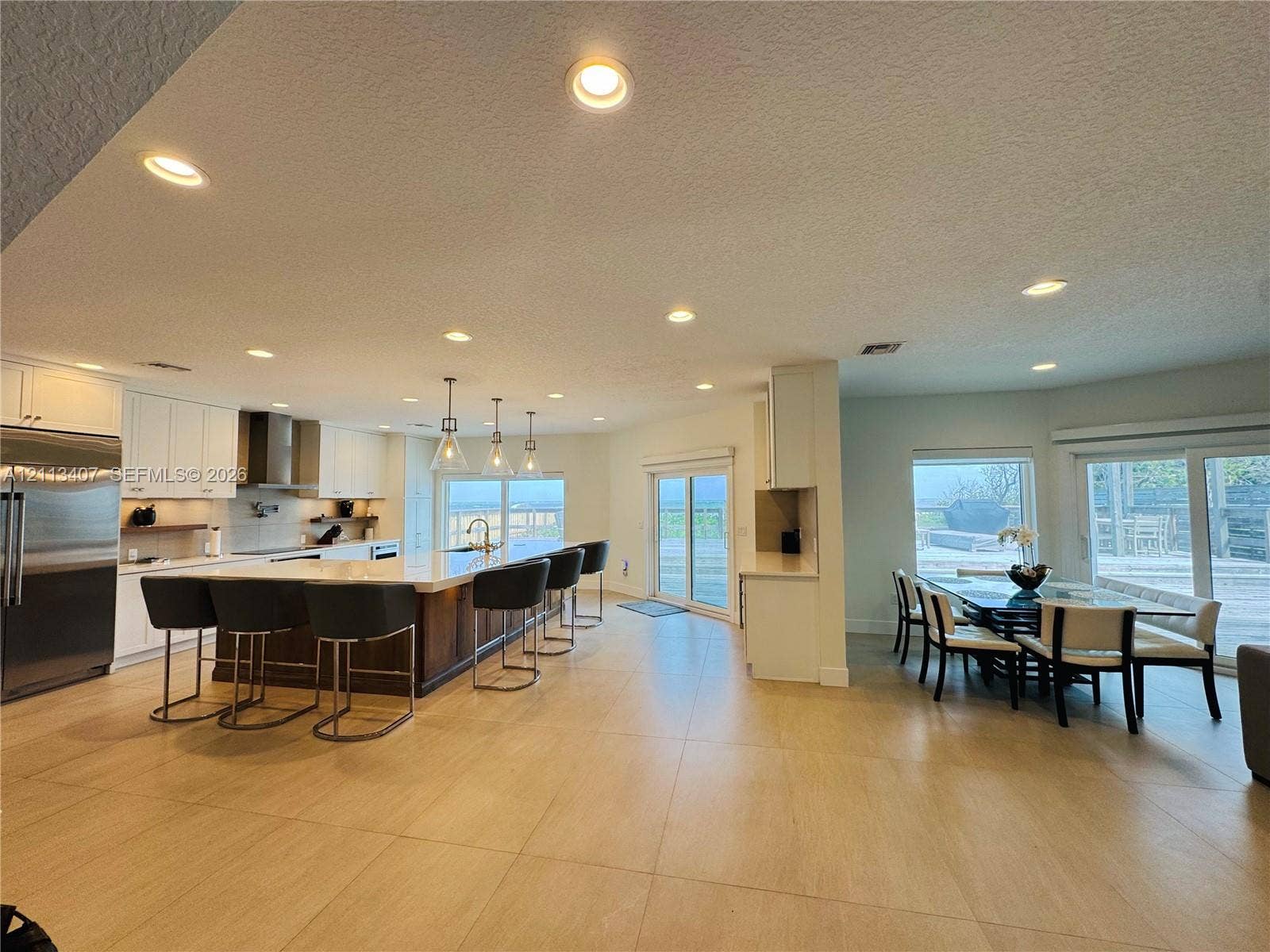 Open-concept interior featuring large-format tile flooring, recessed lighting, white cabinetry, a center island with a stone countertop, and glass sliding doors