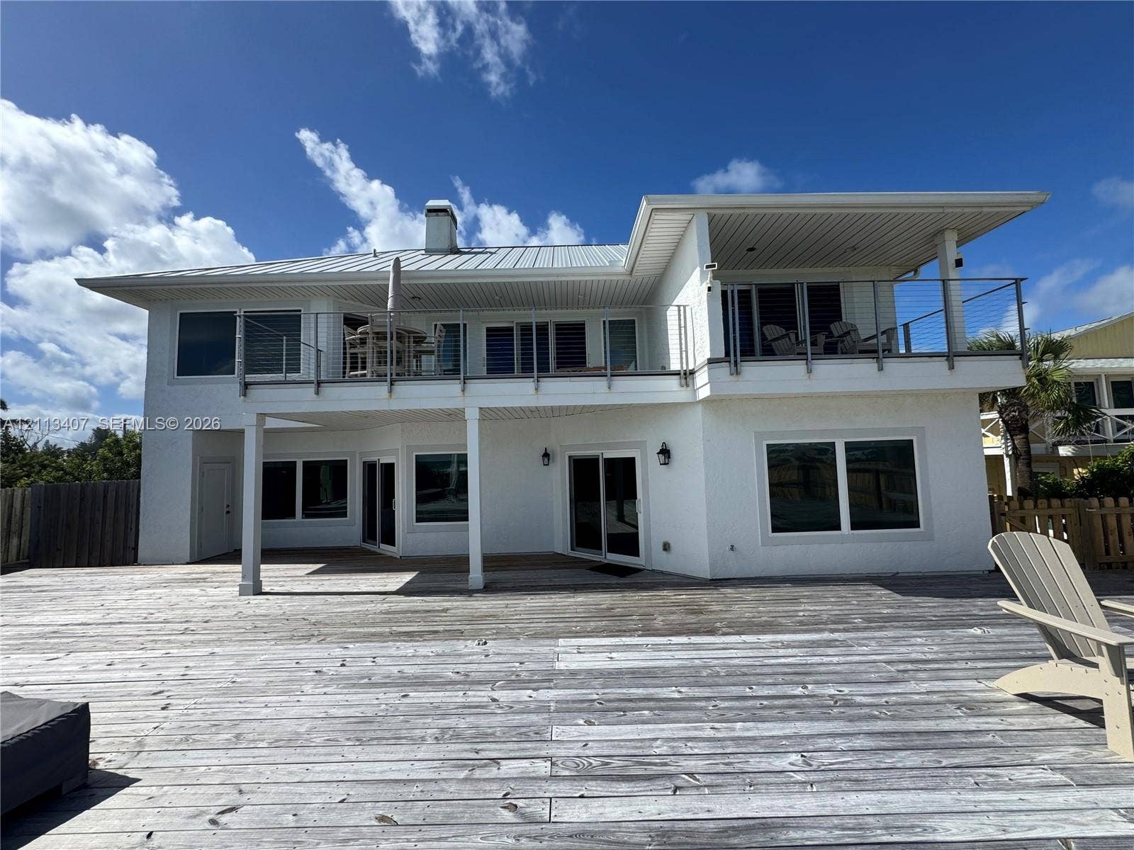 Two-story exterior featuring a metal roof, expansive ground-level wood decking, and a second-level balcony with cable railing