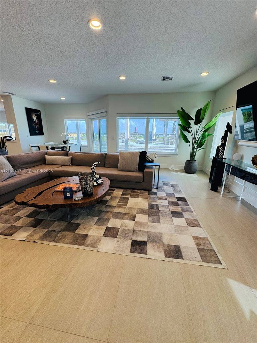 Open-concept interior featuring large-format tile flooring, recessed ceiling lighting, and multiple windows providing natural illumination