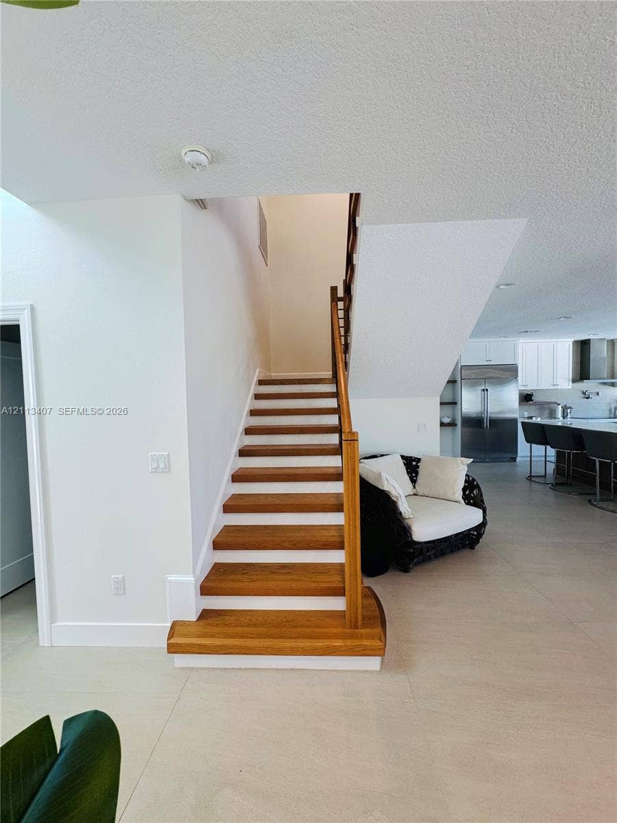Staircase featuring wood treads, white risers, and a wooden handrail, complemented by neutral tile flooring