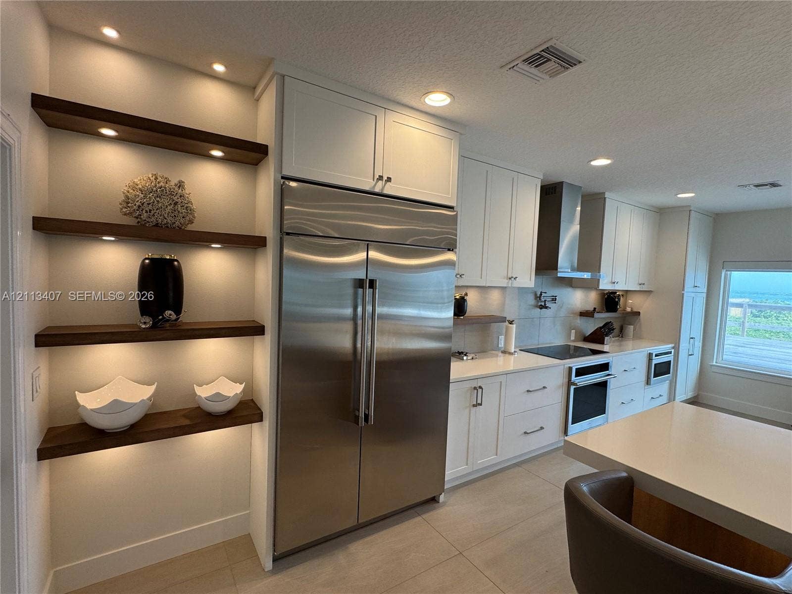 Kitchen featuring recessed lighting, stainless steel refrigerator, white cabinetry, solid-surface countertops, and built-in wood shelving