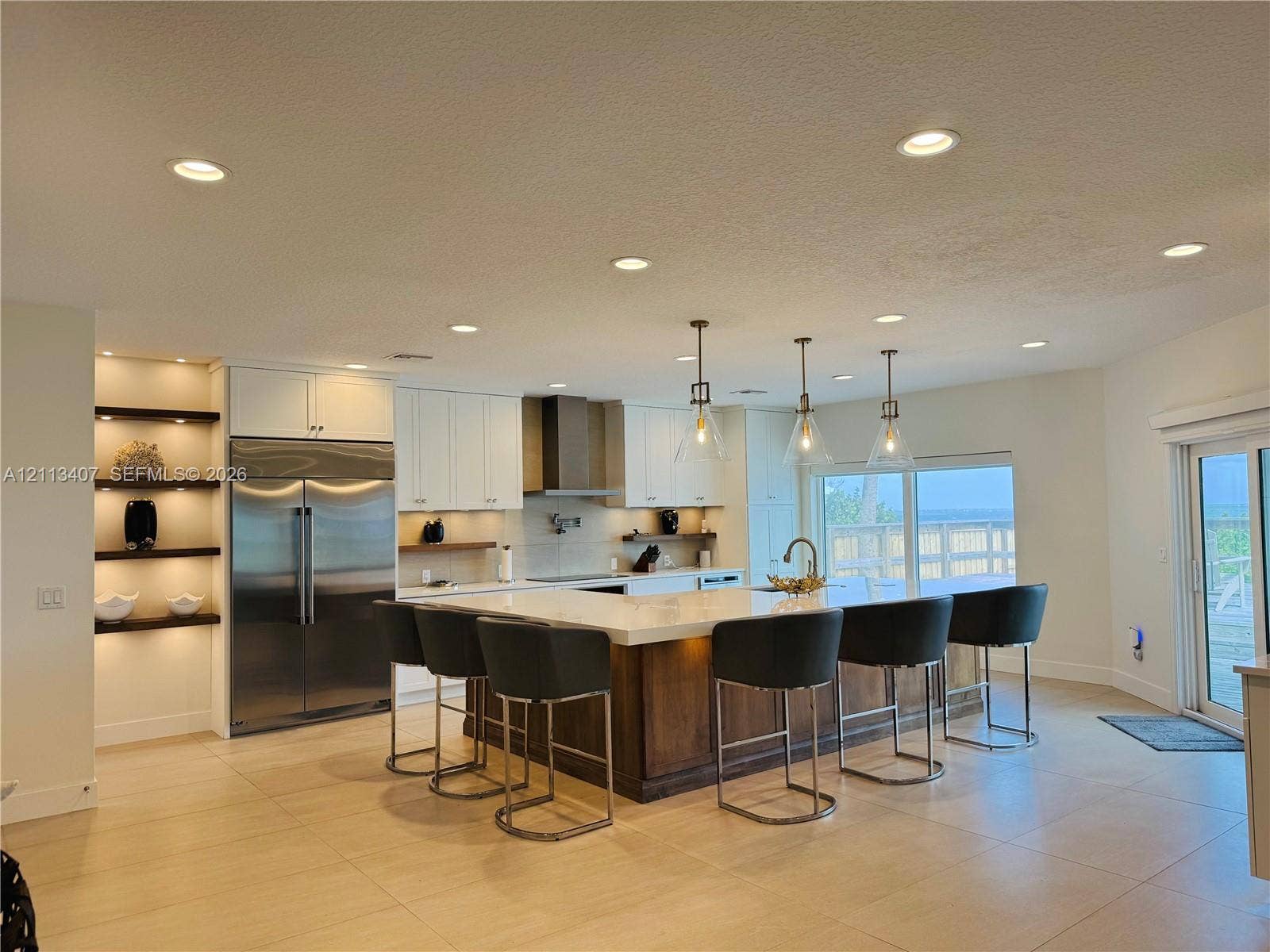 Kitchen featuring a large center island with stone countertop, stainless steel refrigerator, recessed lighting, glass pendant fixtures, and built-in shelving with integrated lighting
