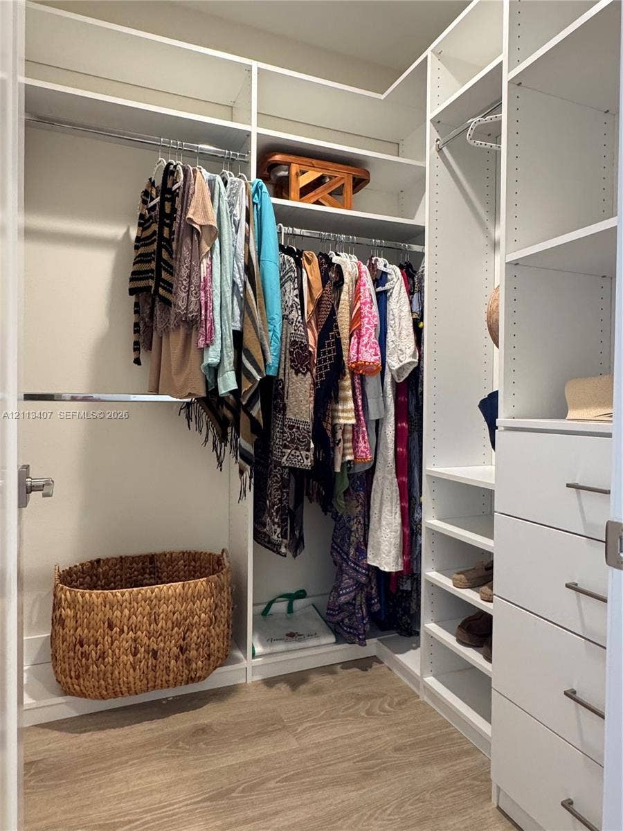 Second floor Walk-in closet featuring custom white shelving, integrated hanging rods, built-in drawer units with metal pulls, and wood-finish flooring