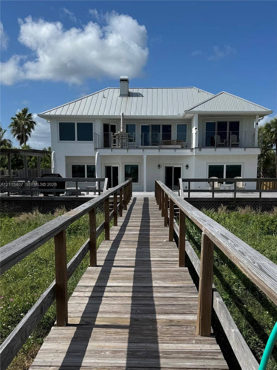 Two-story exterior featuring a metal roof, expansive wood decking, a private elevated walkway, and multiple glass sliding doors