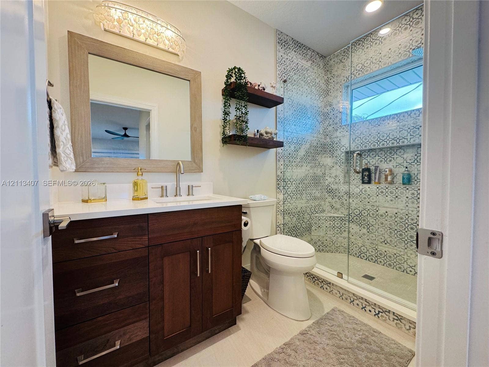 Second floor Dark wood-finish vanity with a white countertop and rectangular undermount sink, patterned tile shower surround, frameless glass shower enclosure, and integrated shower wall niche