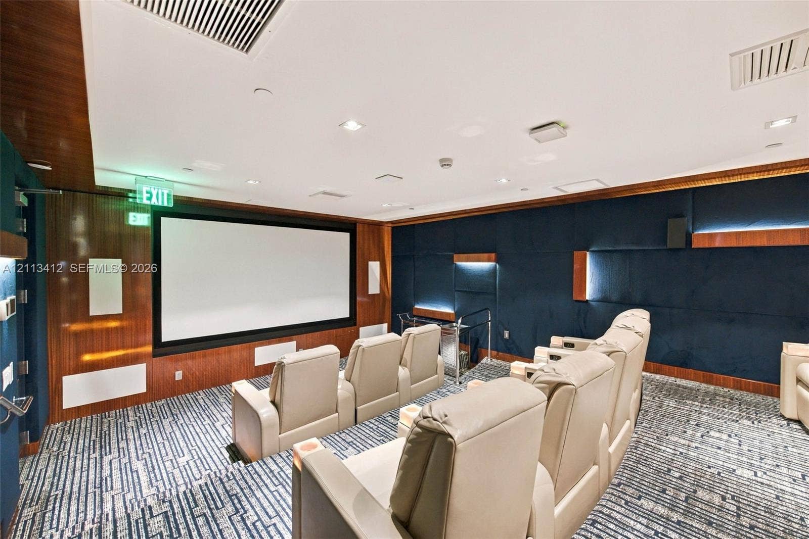 17475 Collins Avenue, #1802, Sunny Isles Beach, FL 33160 Media room featuring tiered flooring, dark blue upholstered wall panels, integrated wood-finish wall accents, recessed lighting, and a built-in projection screen