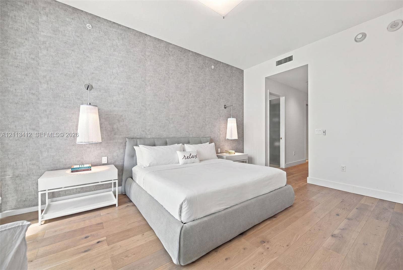 17475 Collins Avenue, #1802, Sunny Isles Beach, FL 33160 Textured gray accent wall featuring dual wall-mounted pendant lights and wide-plank wood-finish flooring