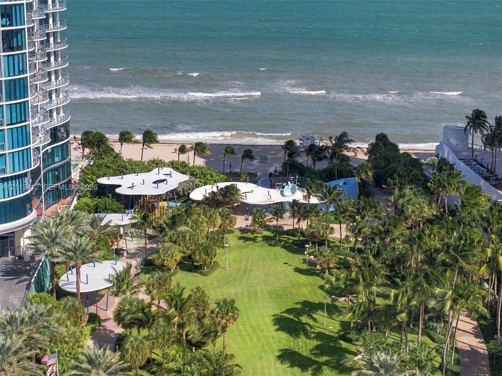17475 Collins Avenue, #1802, Sunny Isles Beach, FL 33160 Expansive coastal grounds featuring manicured green space, mature palm trees, paved walking paths, and organic-shaped shade structures