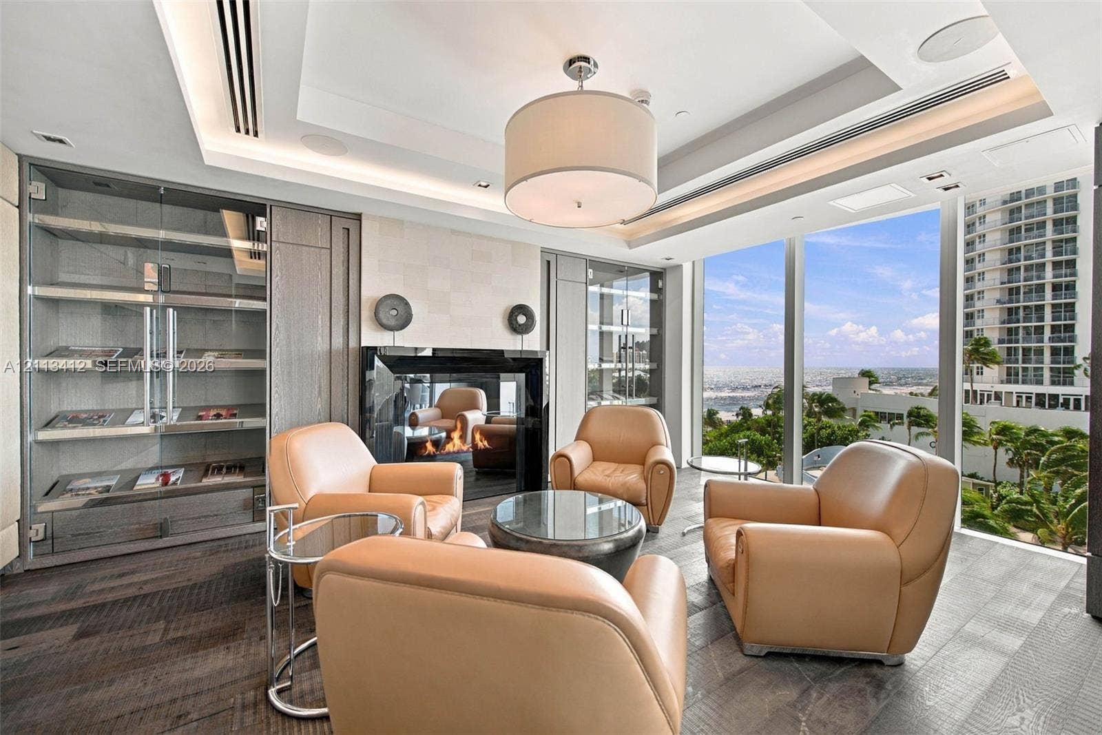 17475 Collins Avenue, #1802, Sunny Isles Beach, FL 33160 Floor-to-ceiling windows, wood-finish flooring, built-in display cabinetry, tray ceiling with recessed lighting, and a modern fireplace with a black glass surround