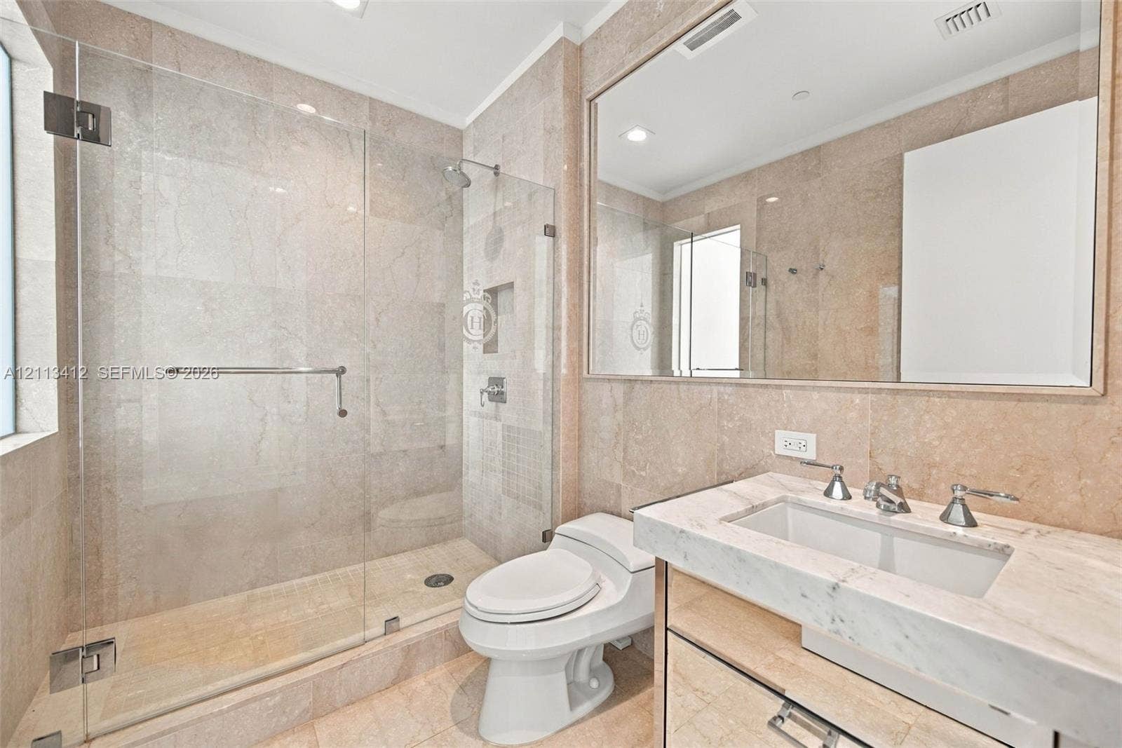 17475 Collins Avenue, #1802, Sunny Isles Beach, FL 33160 Full-wall stone tiling, glass-enclosed walk-in shower with built-in recessed niche, vanity with integrated basin, polished stone countertop, and large framed mirror