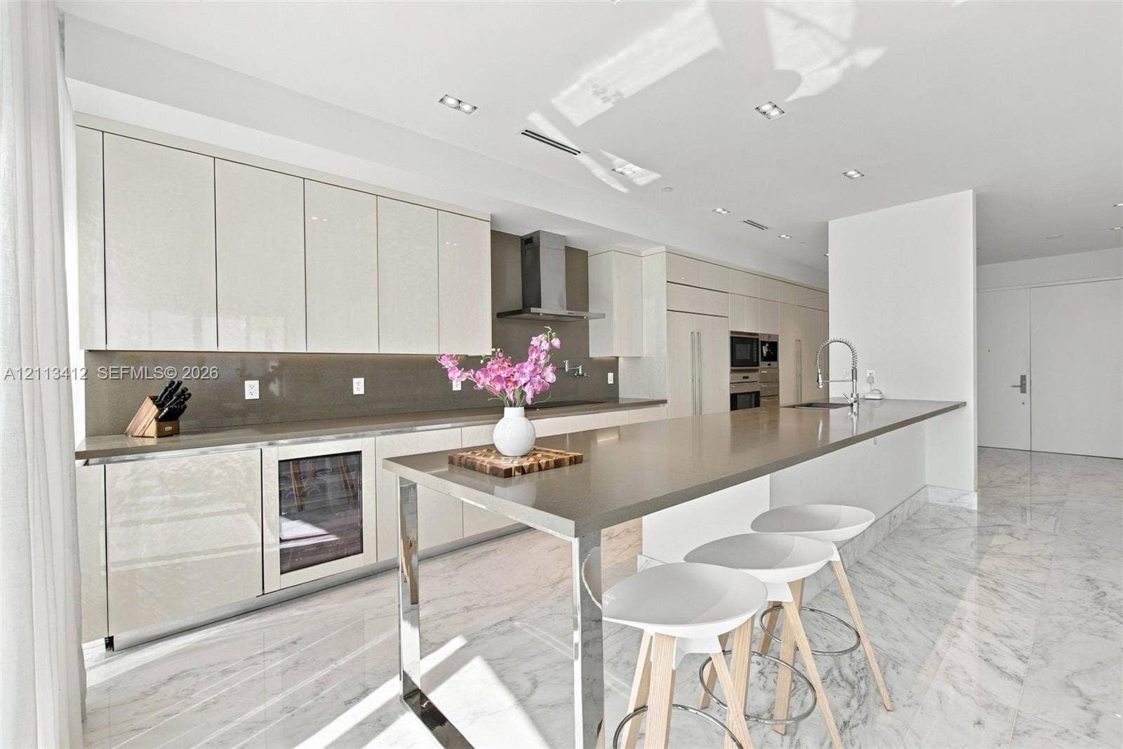 17475 Collins Avenue, #1802, Sunny Isles Beach, FL 33160 Sleek kitchen featuring high-gloss cabinetry, stone-surface countertops, built-in wine refrigeration, stainless steel wall-mounted range hood, and polished stone flooring