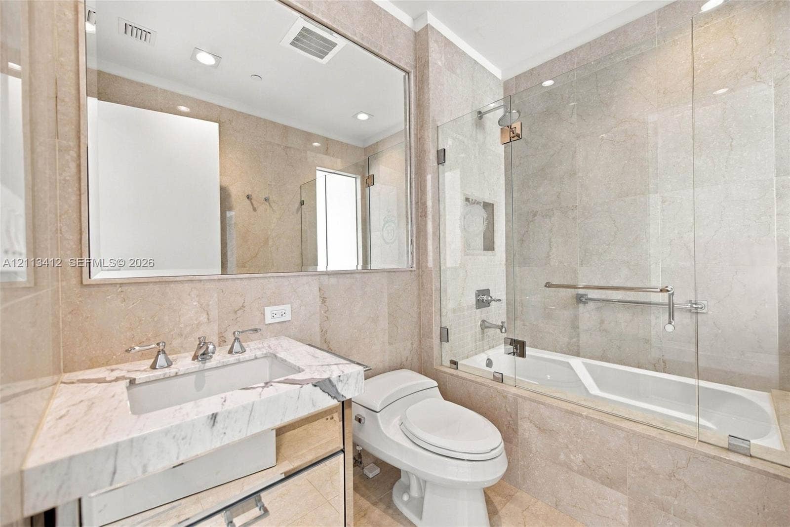 17475 Collins Avenue, #1802, Sunny Isles Beach, FL 33160 Full-height stone wall tiling, custom vanity with a stone countertop and undermount sink, frameless glass shower enclosure, and a large wall-mounted mirror