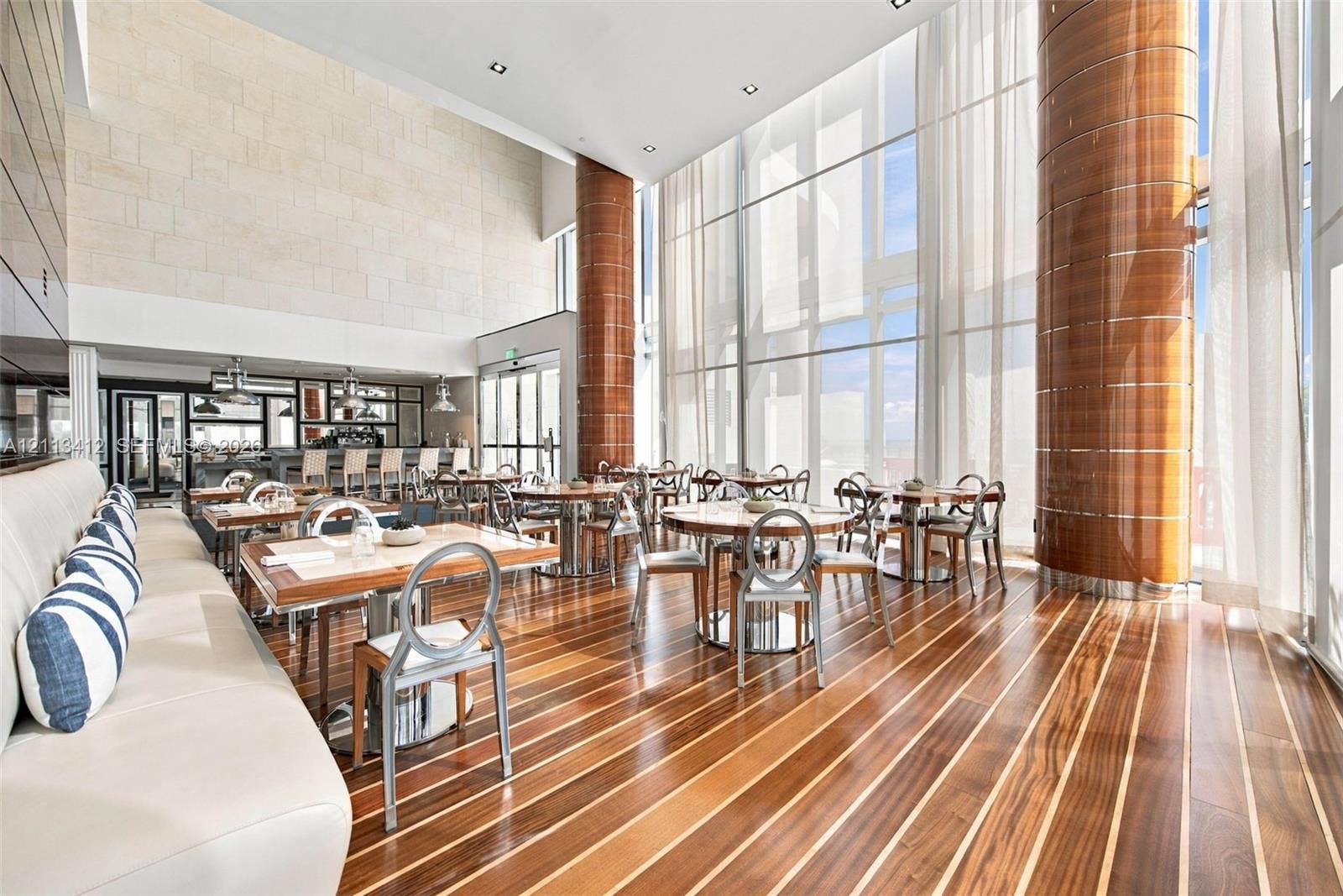 17475 Collins Avenue, #1802, Sunny Isles Beach, FL 33160 Double-height space featuring floor-to-ceiling glass, inlaid wood-finish flooring, decorative cylindrical columns with wood-toned cladding, and textured stone accent wall