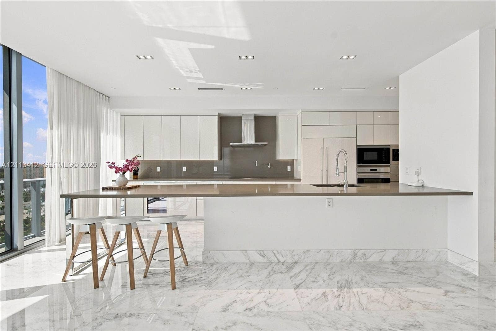 17475 Collins Avenue, #1802, Sunny Isles Beach, FL 33160 Gourmet kitchen featuring high-gloss cabinetry, stone-surface breakfast bar, built-in stainless steel appliances, recessed ceiling lighting, and polished stone tile flooring